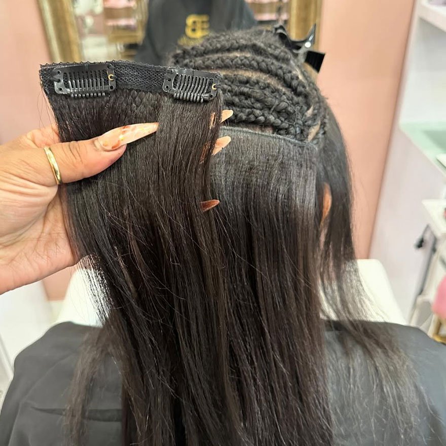 Close-up of a hairstylist applying clip-in hair extensions to cornrow braids on a client&rsquo;s head.