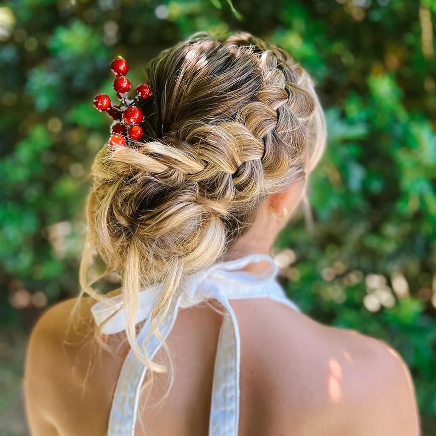 Braided low bun hairstyle decorated with a red berry hair accessory.