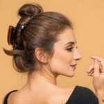 Woman wearing a claw clip updo hairstyle, shown in side profile with a soft, natural makeup look on a warm background.