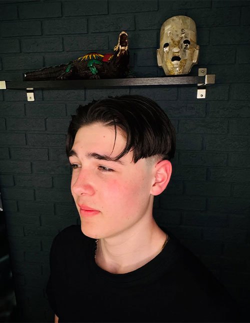 Teen with a 90s-inspired mushroom cut featuring a longer textured top that falls forward and a modern undercut with closely clipped sides.