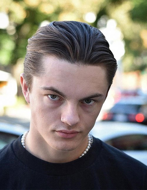 Man with a 90s-inspired undercut, featuring longer hair on top brushed straight back with a smooth, matte finish and shorter, neatly trimmed sides.