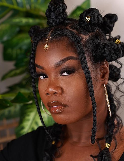 Close-up portrait of a woman with bantu knots styled across the head, with two long face-framing braids and gold hair cuffs.