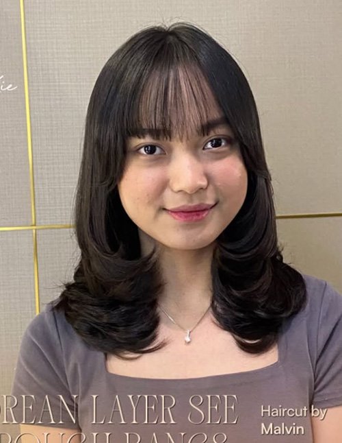 Woman with barely-there wispy bangs and shoulder-length layered hair.