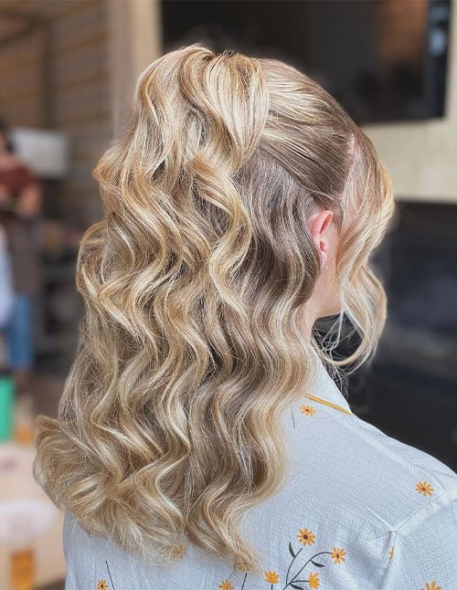 Back view of medium-length blonde hair styled in a half-up ponytail with soft, defined glam waves and a smooth, lifted crown.