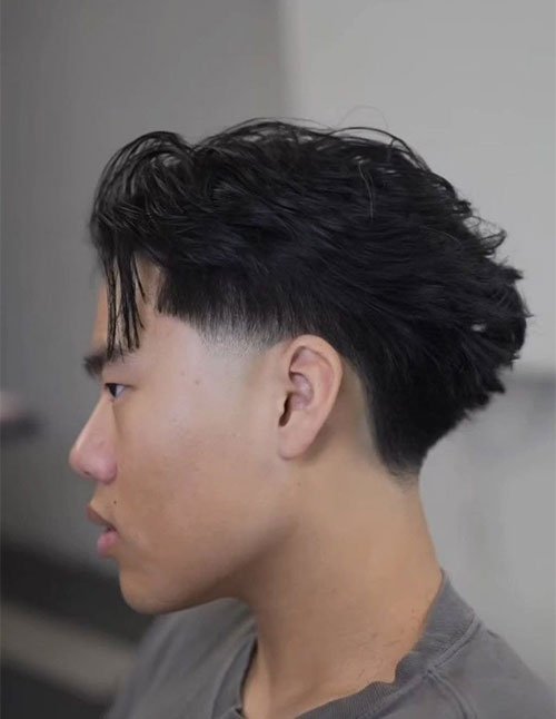 Side profile of a man with a blowout taper fade, featuring longer, voluminous hair on top and a soft taper around the temples and nape.