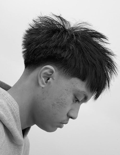 Side-profile of a man with a blowout taper haircut, featuring a textured, lifted top and a clean taper fade around the sides.
