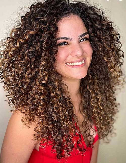 Smiling woman with big, voluminous curly hair and warm caramel highlights, wearing a red top.