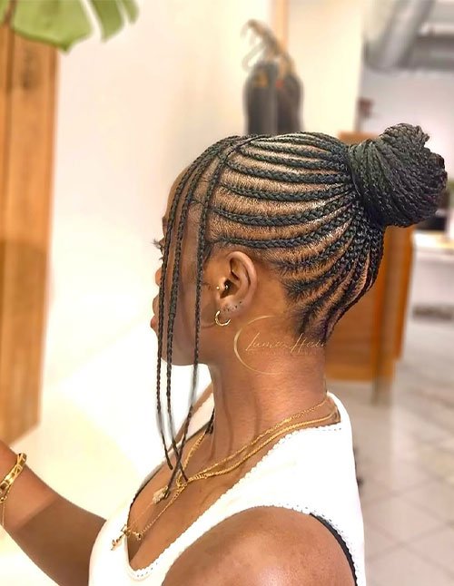 Side view of a woman with cornrow braids styled into a braided bun at the back, with a few thin braids left out in front.