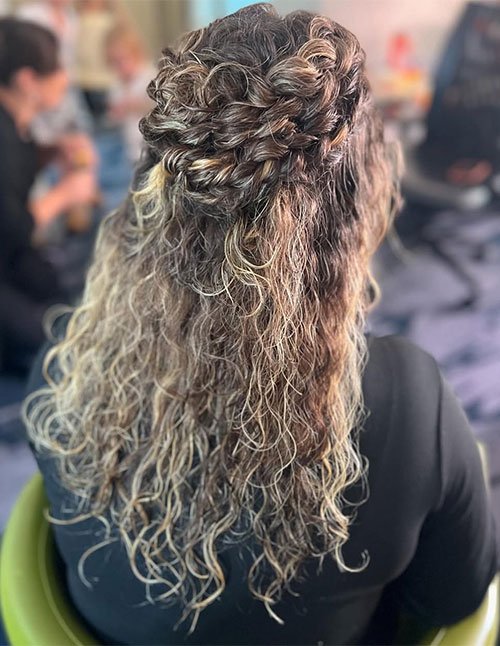 Back view of wavy hair styled half-up with an intricate braided crown across the back and loose textured waves below.
