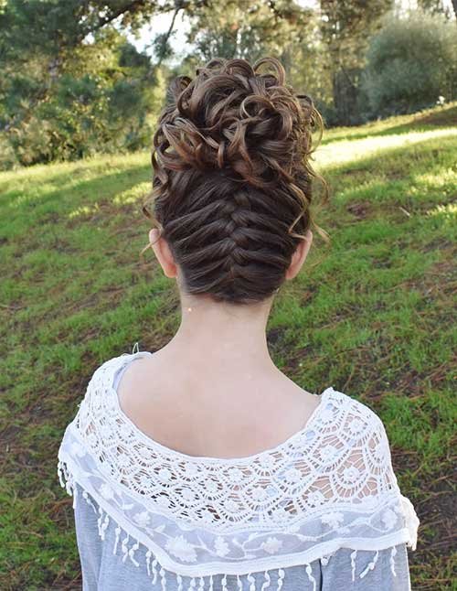 Upside-down French braid from the nape into a high curly bun, shown from the back outdoors.