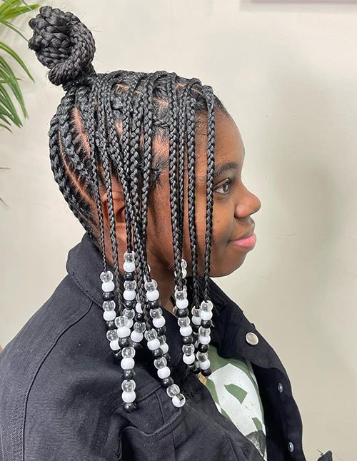 Side profile of a braided formal knot bun featuring neat box braids gathered into a high knot bun, with black-and-white beaded ends framing the face.