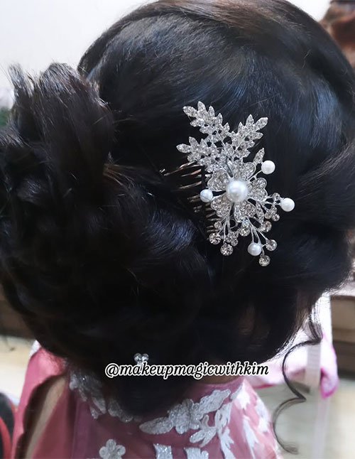Close-up of a low bun updo with smooth, voluminous sections, finished with a sparkling floral hair comb featuring pearls and rhinestones.