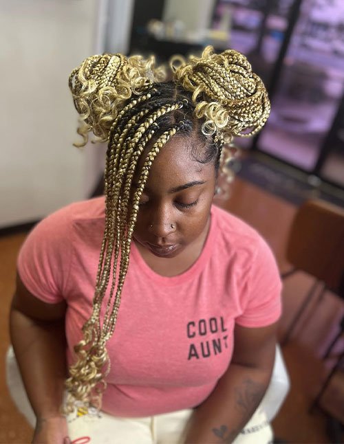 Golden-blonde braids styled into two high space buns with loose curly ends and a long braided fringe falling to the front.