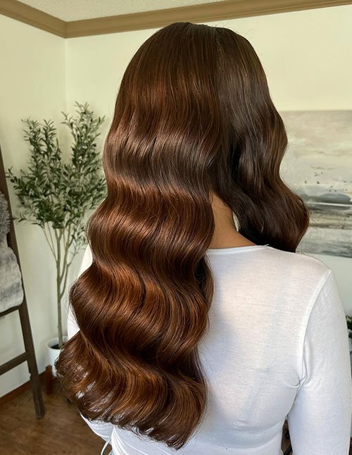 Back view of long brunette hair styled in smooth, glossy glam waves with defined S-shaped bends and a polished, wedding-ready finish.