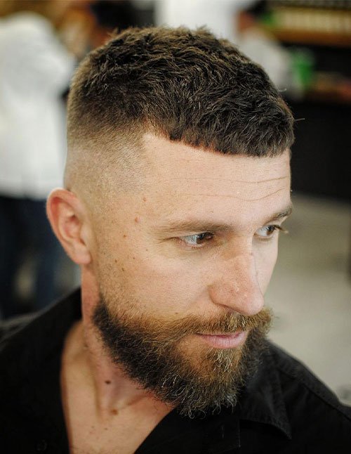 Man wearing a Caesar fade haircut with a short, textured top and forward fringe, paired with a clean fade on the sides and back.