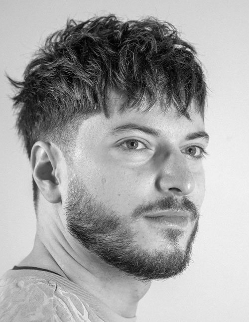 Man with choppy fringe hairstyle featuring textured front bangs and faded sides.