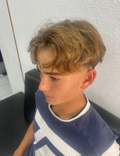 Young boy with a classic 90s curtains haircut, featuring a clean middle part, long layered sides, and soft natural waves framing the face.