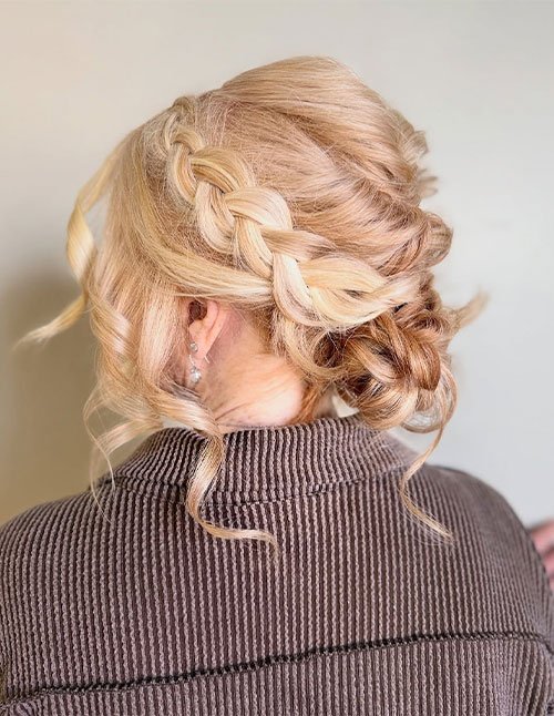 Classic braided updo with a soft side braid flowing into a low, loose bun, finished with face-framing curls.