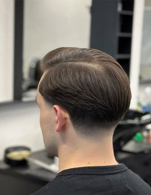 Man wearing a classic side-swept taper haircut with neatly combed hair on top and a smooth, low taper at the back for a timeless old money look.