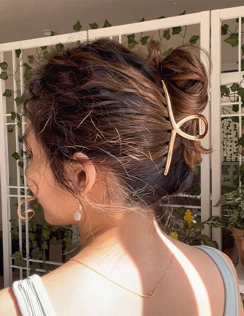 Side view of a woman with a messy updo secured with a large gold claw clip, with loose face-framing strands.