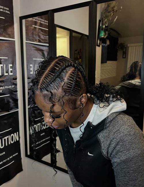 Criss-cross cornrow braids styled neatly across the scalp, finished with soft, defined curly ends and loose tendrils framing the face.