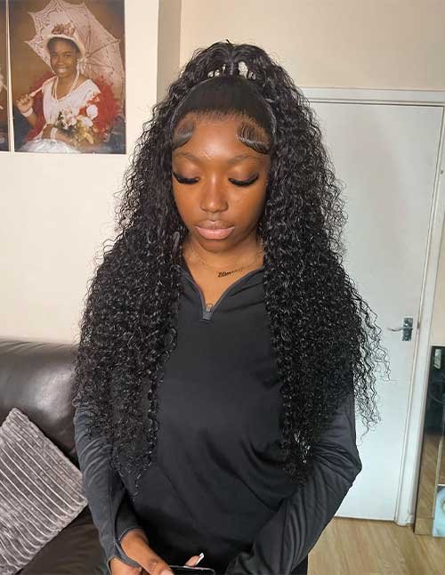 Front view of long curly hair styled half-up in a top knot with defined baby hairs.