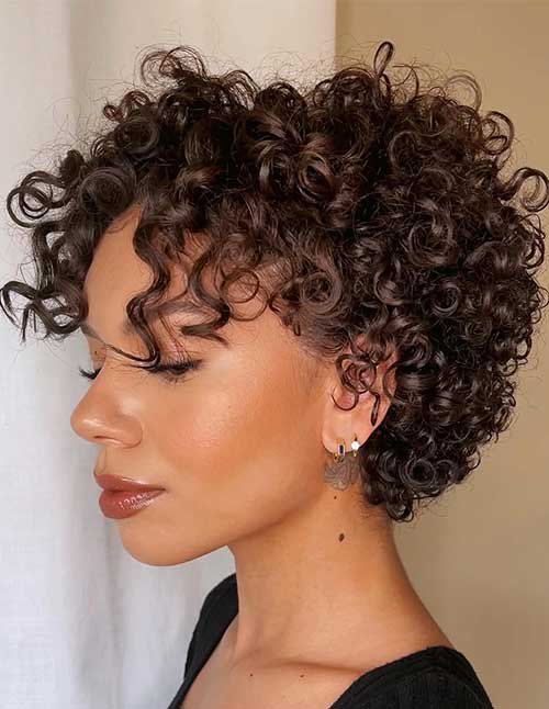 Side-profile of a woman with a short curly pixie cut featuring tight ringlets and soft curly fringe.