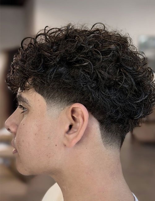 Man with a curly taper fade hairstyle featuring natural curls on top and clean faded sides.