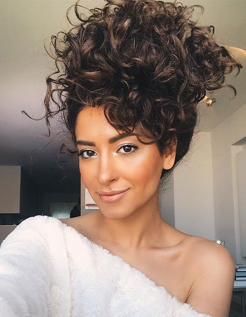 Woman wearing a high curly top bun with loose curls and lots of volume.