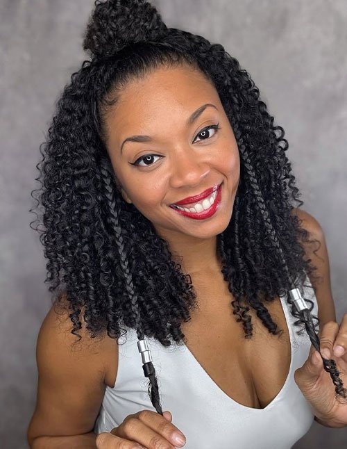 Woman smiling with a curly top knot bun and defined natural curls, featuring two face-framing braids with hair cuffs.