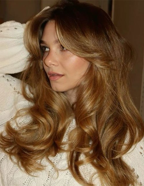 Close-up of long layered hair styled in a bouncy 90s blowout with big curls, lifted roots, and soft face-framing pieces.