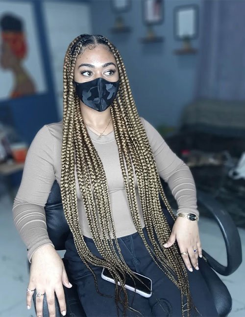 Cute golden box braids in an extra-long length with a center part, styled sleek at the roots and flowing over the shoulders.