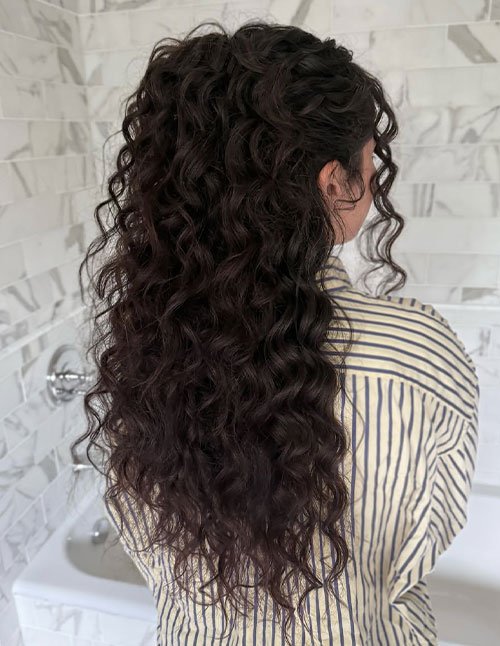 Girl with long curly hair styled in a cute half-up hairstyle, featuring defined natural curls flowing down the back.