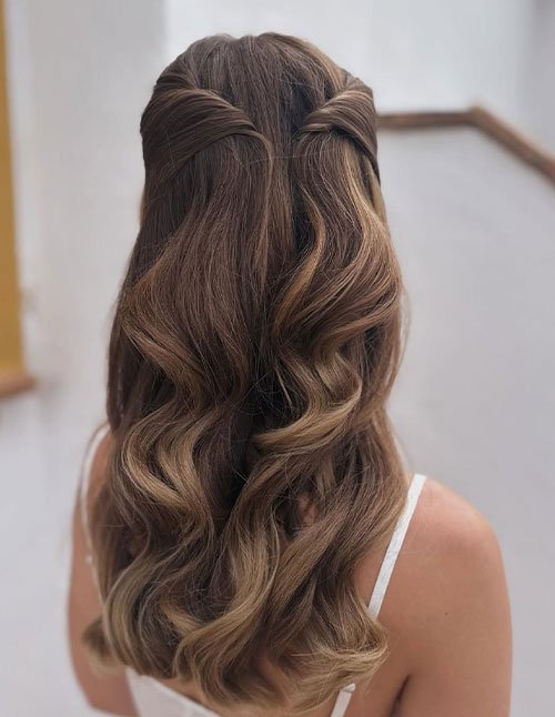 Back view of a cute quick hairstyle with medium-length hair styled in a soft half-up twist and loose waves.
