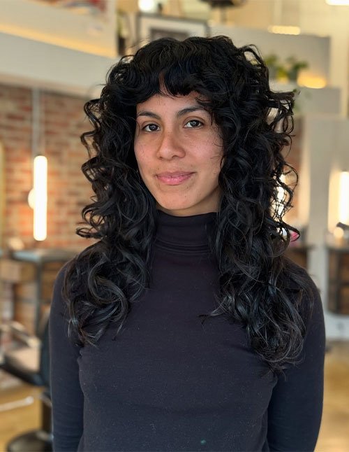 Dark voluminous curls with textured bangs and long layered shape