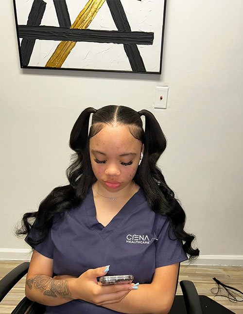 Woman with a center part and two high ponytails, styled into long, loose glossy curls that fall over both shoulders.