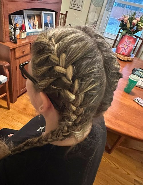 Side view of a woman with blonde-highlighted hair styled in a thick Dutch braid starting at the crown and continuing down to the nape.