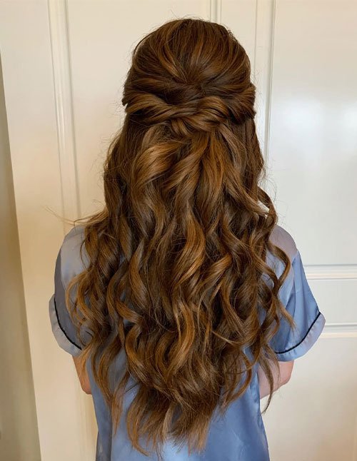 Back view of a woman with thick, long hair styled in an easy half-up hairstyle with soft waves, ideal for formal occasions.
