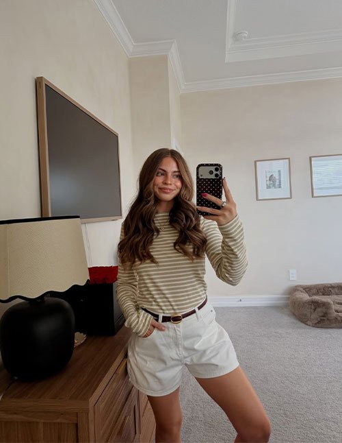 Mirror selfie of a woman wearing one of the easy hairstyles for medium hair, styled with soft, loose waves and a natural middle part.