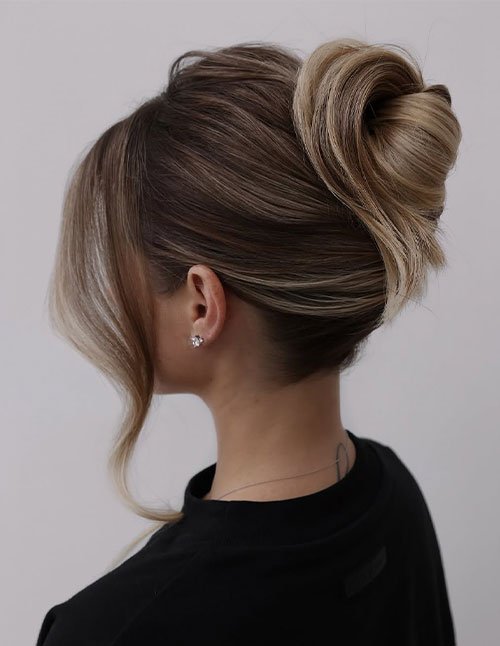 Easy party hairstyle with a sleek high bun and a soft face-framing strand, styled neatly from the side.