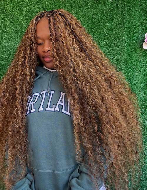 Extra-long goddess braids with braided roots and extremely long, loose curls in a warm honey-brown tone.