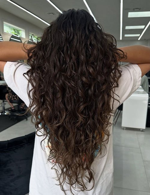 Girl with very long, natural curly hair flowing down the back, styled in loose, airy curls.