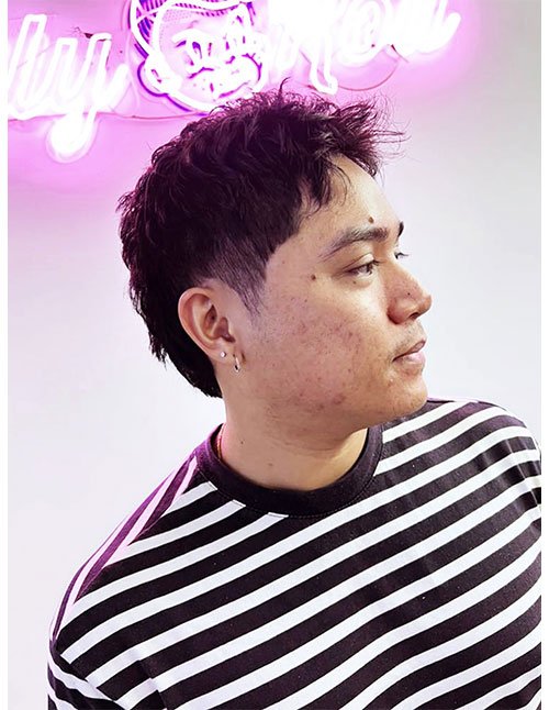 Side profile of a man with a 90s-inspired textured crop, featuring a messy, piecey top and a low taper on the sides, wearing a striped shirt.