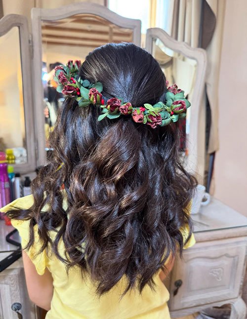 Girl with shoulder-length curly hair styled half-up and decorated with a floral crown across the back of the head.