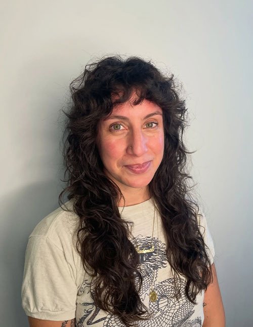 Front view of a woman with long dark hair styled in natural flowing curls, featuring soft layers and wispy bangs.