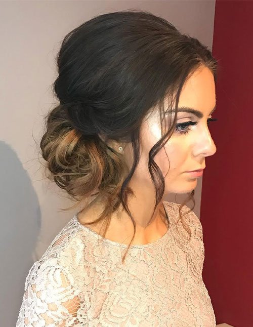 Side view of a woman wearing a formal side bun with softly twisted hair and loose face-framing curls.