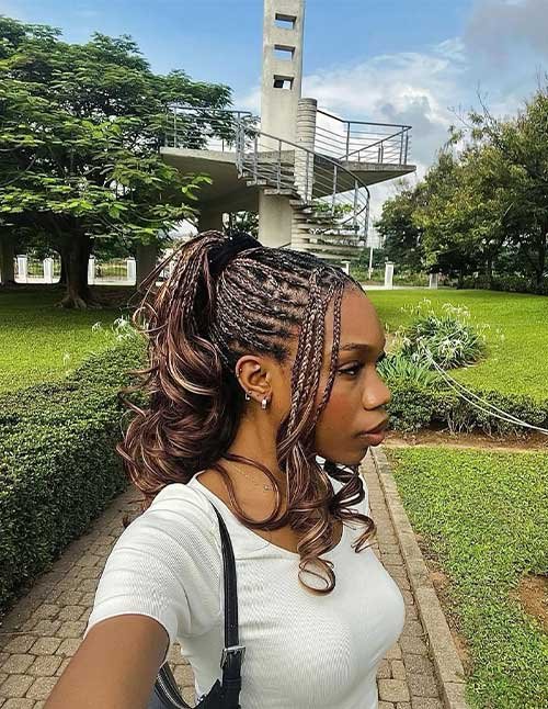 Side-profile of a woman with braided cornrows pulled into a high ponytail with loose, bouncy curls.