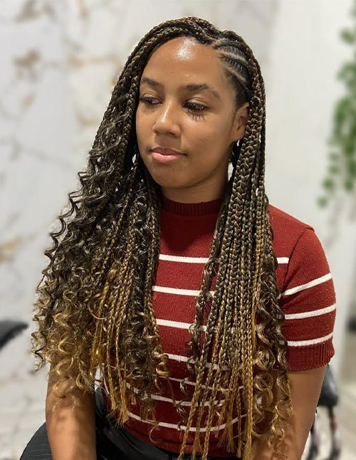 Woman wearing long ombré goddess braids (box braids) with loose curly strands, styled in a side-swept look.