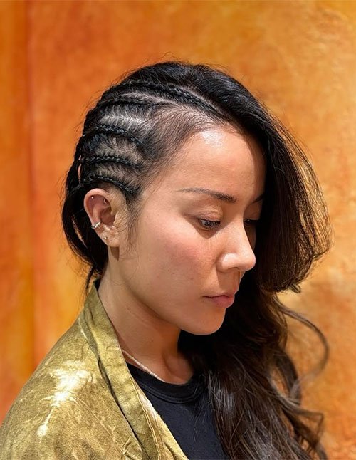 Side profile of a woman wearing a side hair braid style with neat cornrow braids on one side and loose hair swept to the other.