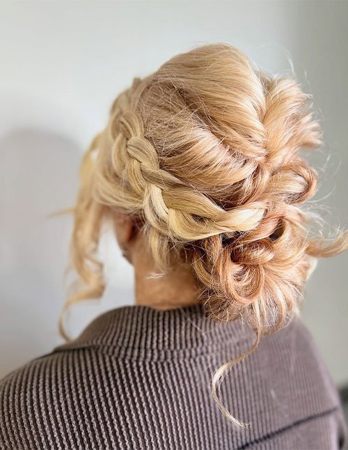 Back view of a hair braid textured bun featuring a loose side braid woven into a soft, messy low bun.